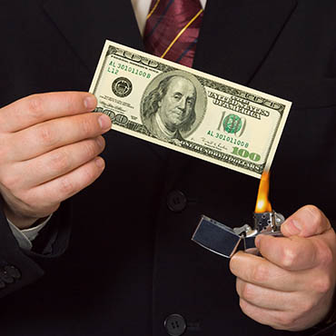 Shutterstock image (by Tatiana Popova): businessman burning money with a lighter.