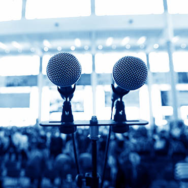 Shutterstock image (by hxdbzxy): closeup microphone in an auditorium of people.